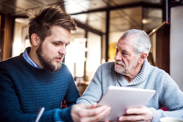 An adult son discussing financial plans on a tablet with his retired father.